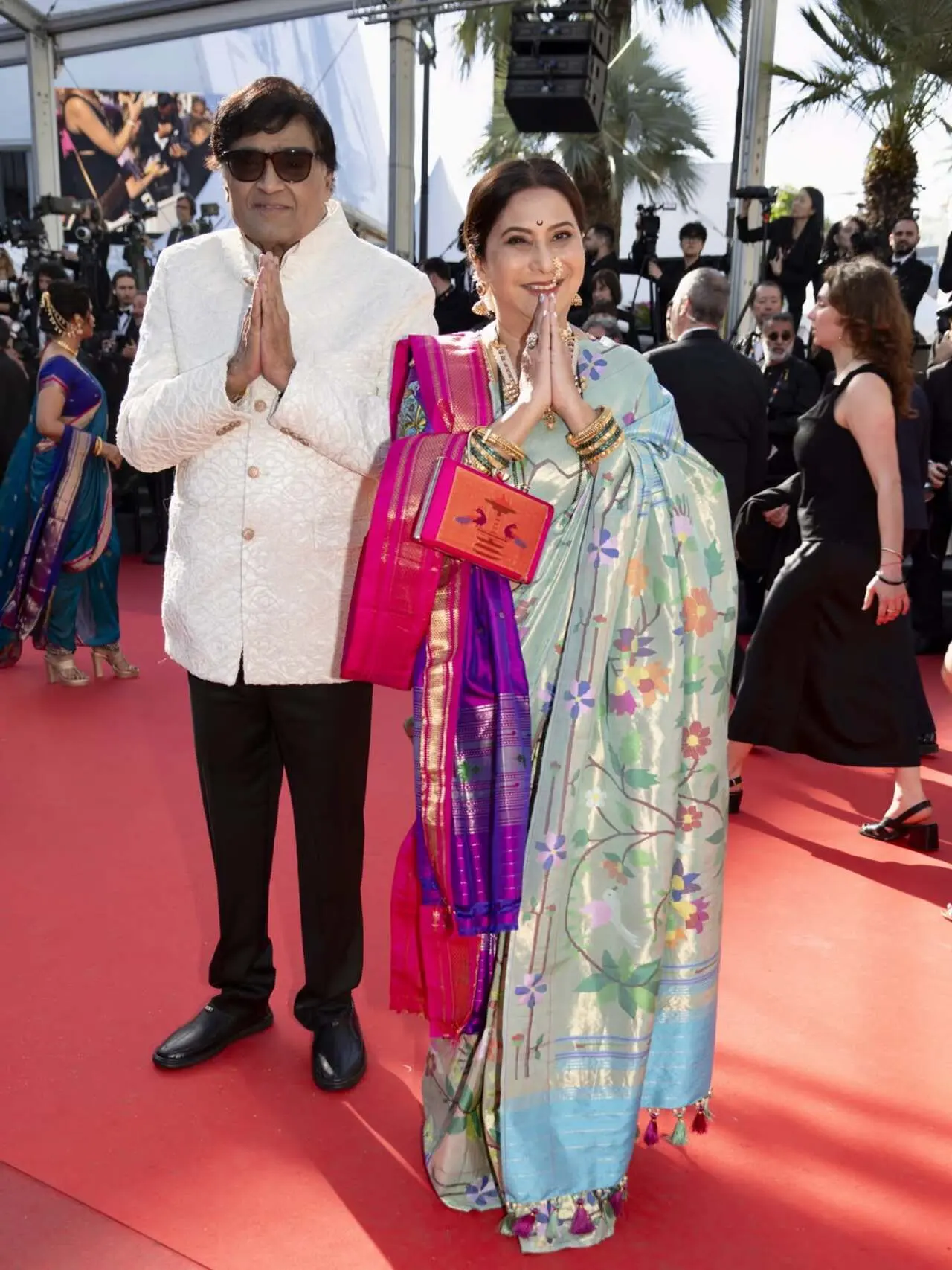 At the 2026 Cannes Film Festival, veteran Marathi superstar Ashok Saraf and his actress-wife Nivedita Saraf chose traditional Maharashtrian attire for their historic red carpet debut. Representing regional Indian cinema on the global stage, Ashok Saraf looked highly dignified in a sophisticated, timeless ivory bandhgala coat paired with classic black trousers. Complementing him, Nivedita Saraf stunned in a traditional handwoven Paithani silk saree featuring intricate floral motifs and rich zari borders, layered elegantly with a matching festive zari-work shawl. She completed her classic aesthetic with a traditional gold Marathi Nath, a customary bindi, a fresh floral gajra, and a matching custom Paithani handbag At the 2026 Cannes Film Festival, veteran Marathi superstar Ashok Saraf and his actress-wife Nivedita Saraf chose traditional Maharashtrian attire for their historic red carpet debut. Representing regional Indian cinema on the global stage, Ashok Saraf looked highly dignified in a sophisticated, timeless ivory bandhgala coat paired with classic black trousers. Complementing him, Nivedita Saraf stunned in a traditional handwoven Paithani silk saree featuring intricate floral motifs and rich zari borders, layered elegantly with a matching festive zari-work shawl. She completed her classic aesthetic with a traditional gold Marathi Nath, a customary bindi, a fresh floral gajra, and a matching custom Paithani handbag